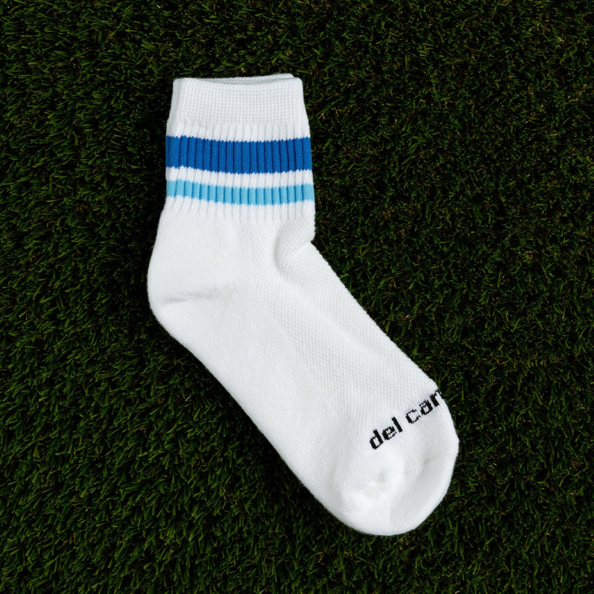 Del Campo Golf white crew sock with blue stripe detail on grass background | product, on-course