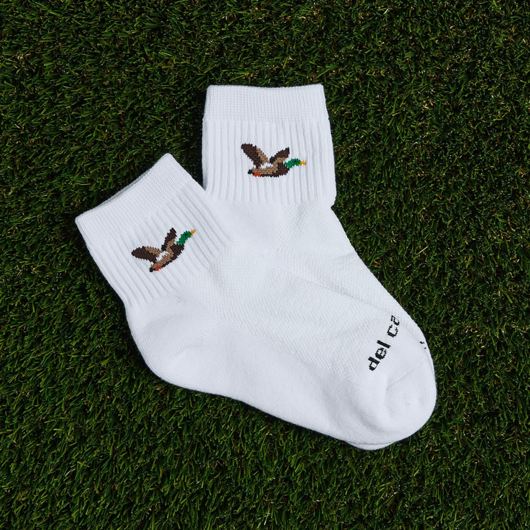 Pair of Del Campo Mallard socks with flying duck logo laid on grass