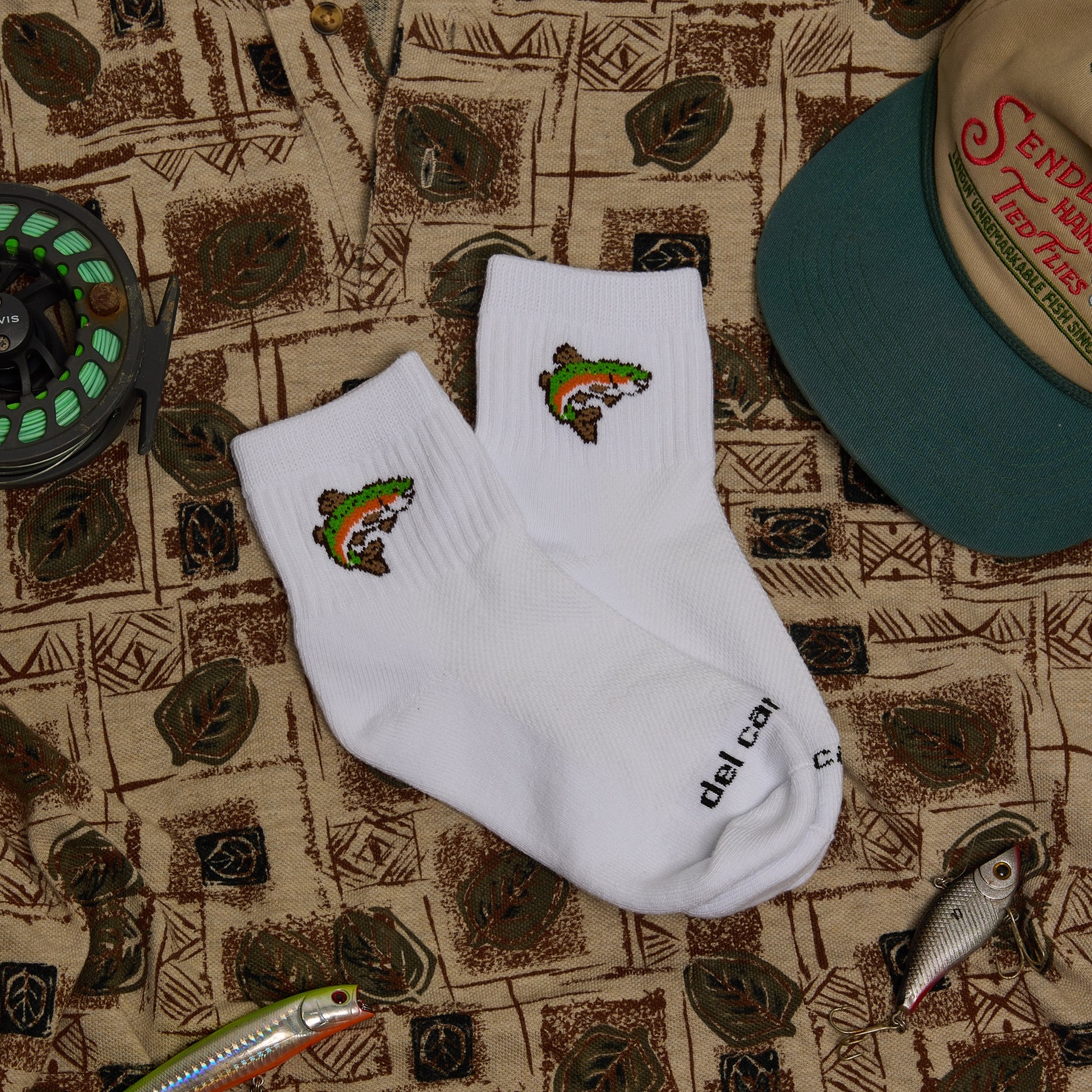 Pair of Del Campo Trout socks on a patterned bandana with a hat and fishing lures