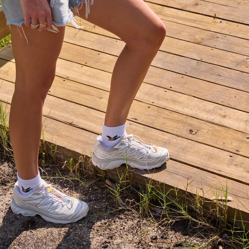 Woman stepping onto a boardwalk wearing white sneakers and Del Campo Mallard socks