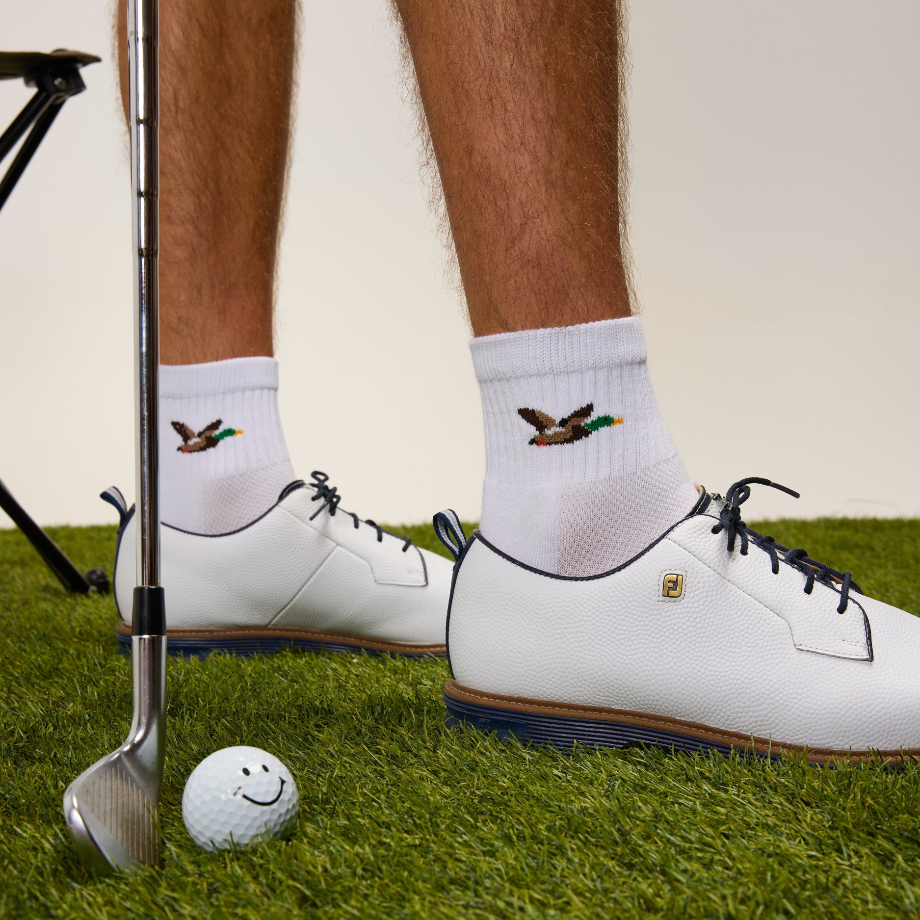Del Campo Mallard sock worn with a white golf shoe, club and smiley golf ball on grass