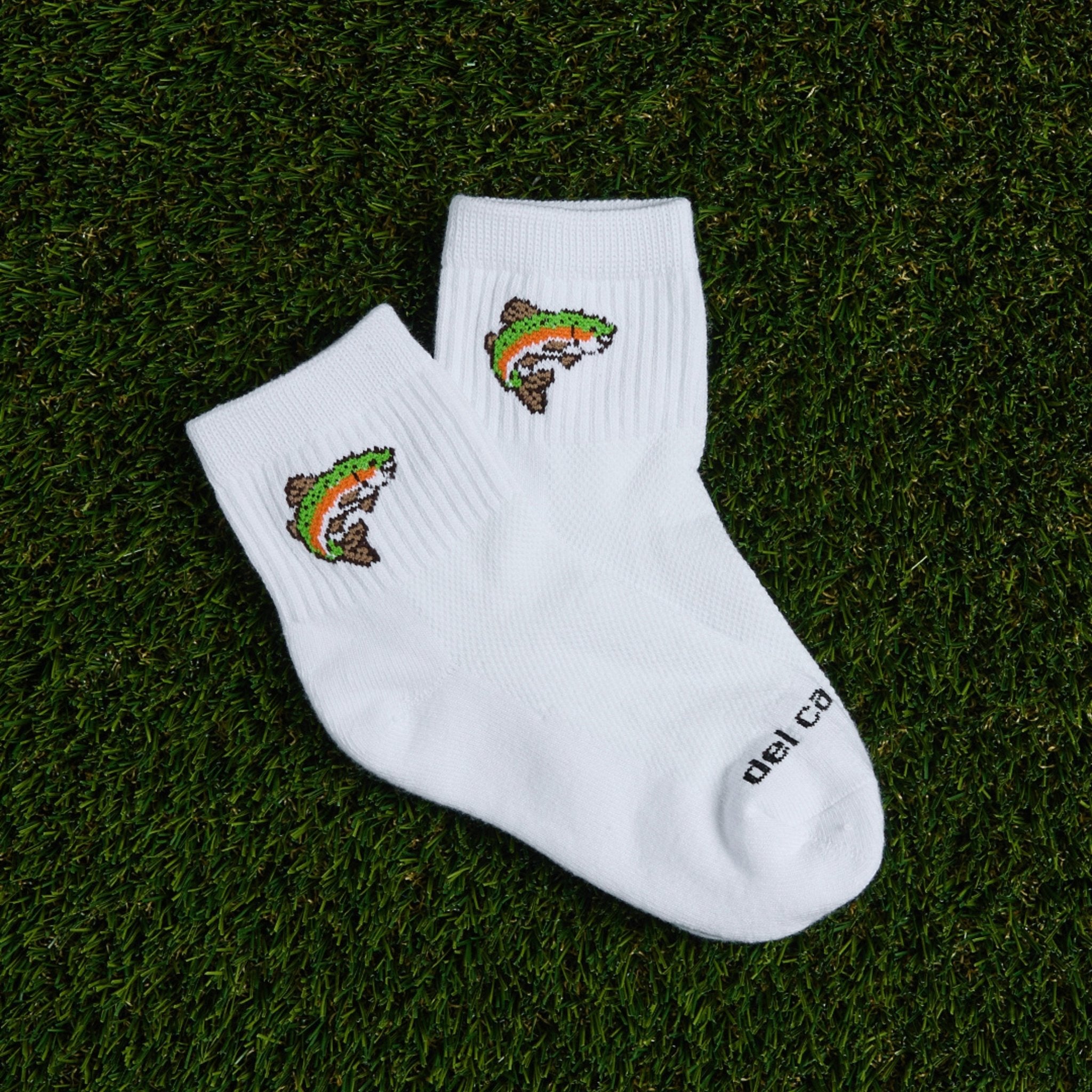 Pair of Del Campo Trout socks with rainbow trout logo laid on grass