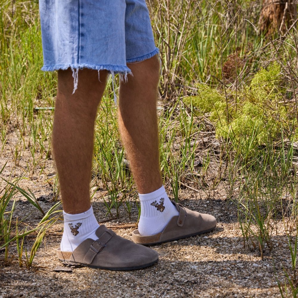 Man on a gravel trail wearing Del Campo Whitetail Deer socks with clogs