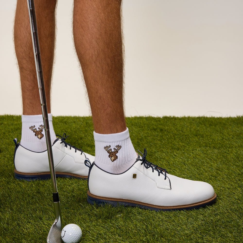 Del Campo Whitetail Deer socks worn with white golf shoes, a club and ball on grass