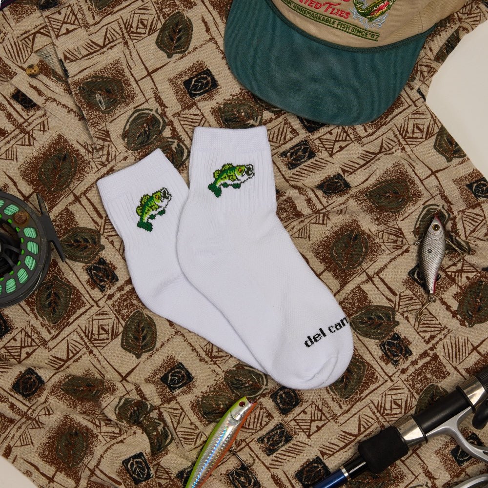 Pair of Del Campo Largemouth Bass socks on a patterned bandana with a hat and fishing gear