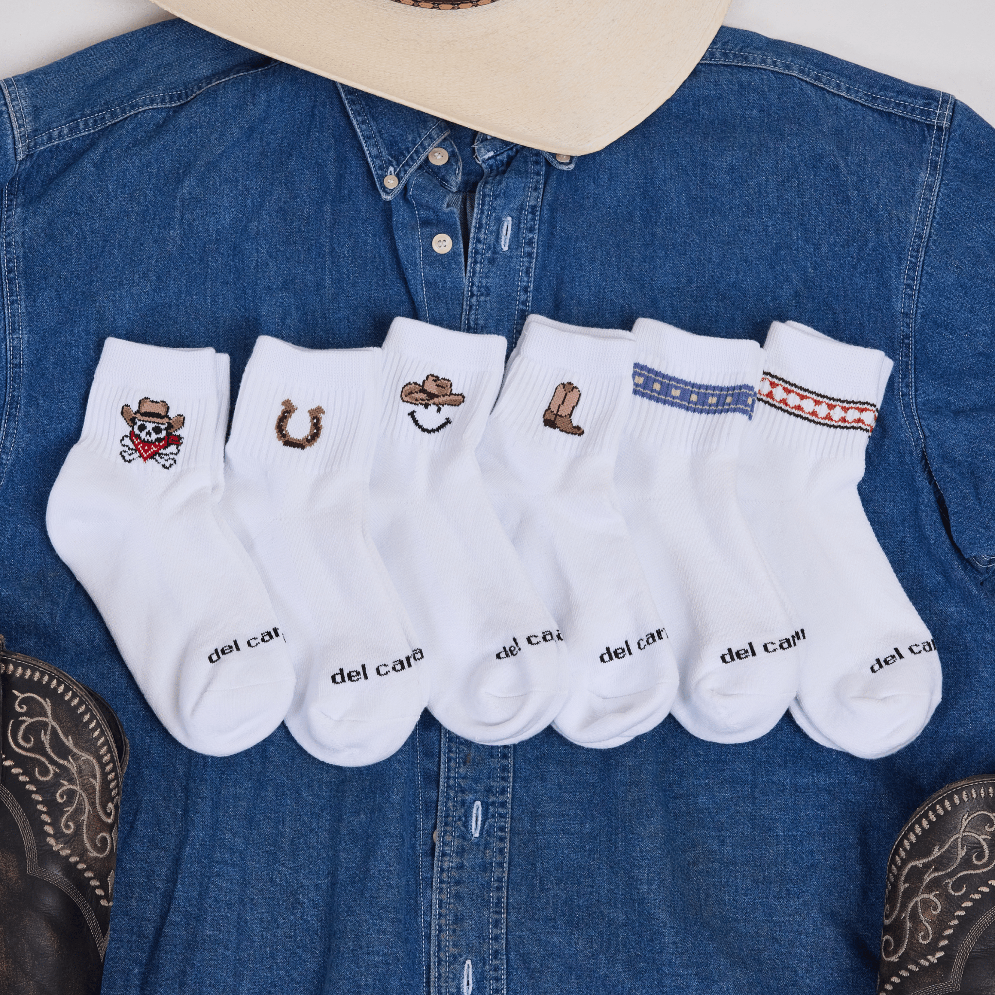 Del Campo Western Pack socks arranged on a denim shirt with a cowboy hat, showing all six western designs.