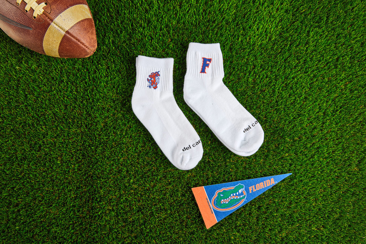 Both officially licensed Del Campo Florida Gators socks on the turf with a football and a Florida pennant.