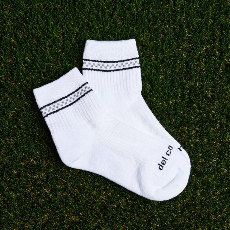 Del Campo Golf white crew socks with black and grey checkered stripe pattern, displayed on grass. | product, on-course