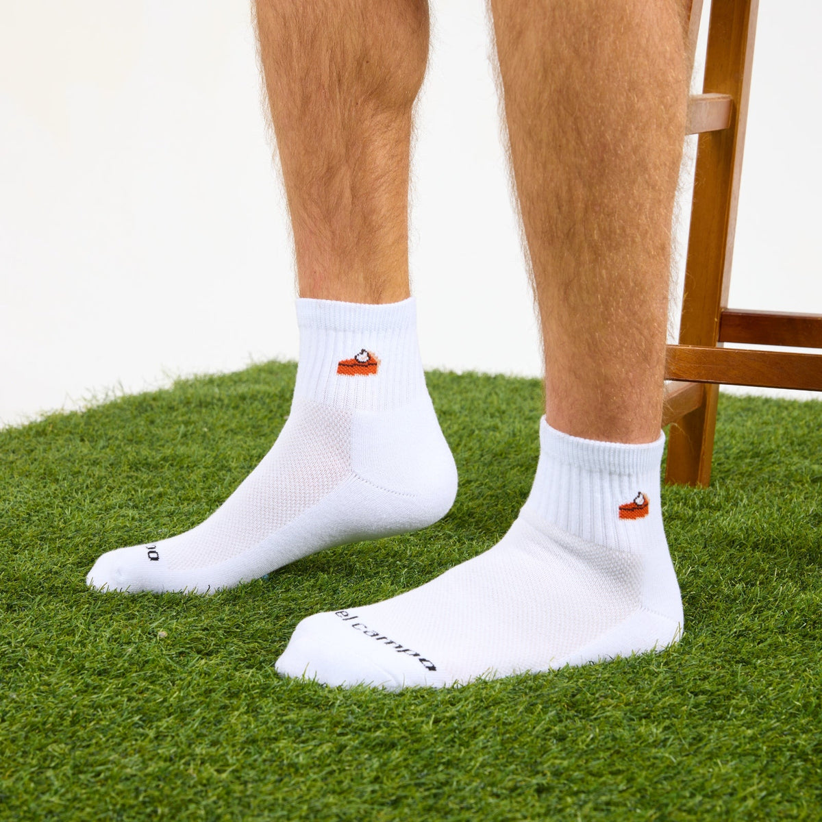 Del Campo Pumpkin Pie Thanksgiving golf socks, white quarter socks with a knit slice of pumpkin pie, worn on the grass, one foot forward