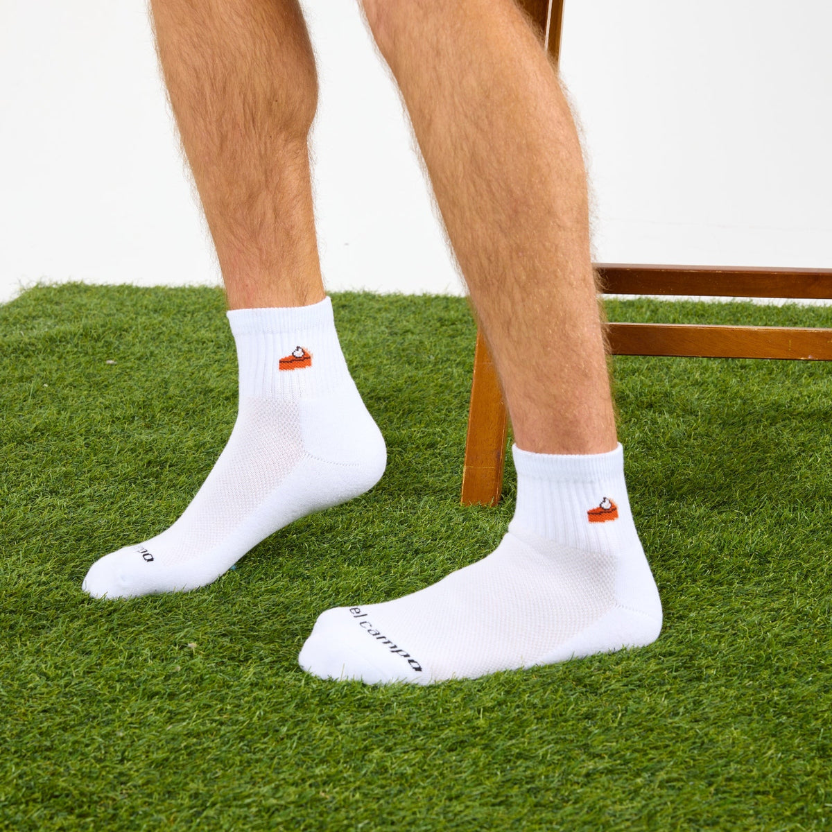 Del Campo Pumpkin Pie Thanksgiving golf socks, white quarter socks with a knit slice of pumpkin pie, worn on the grass by a wooden stool