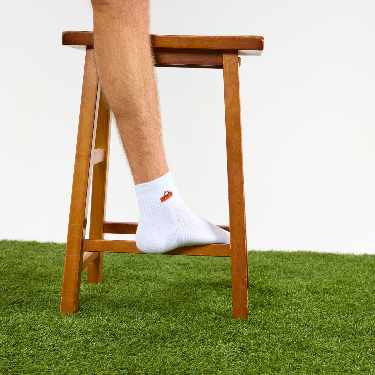 Del Campo Pumpkin Pie Thanksgiving golf socks, white quarter socks with a knit slice of pumpkin pie, worn with one foot up on a wooden stool