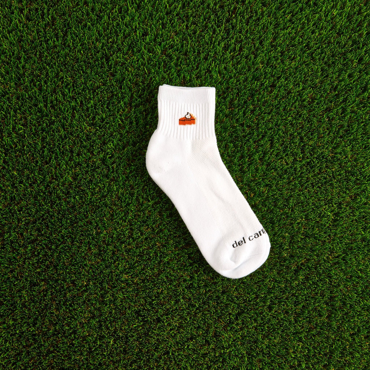 Del Campo Pumpkin Pie Thanksgiving golf socks, white quarter socks with a knit slice of pumpkin pie, single sock on grass