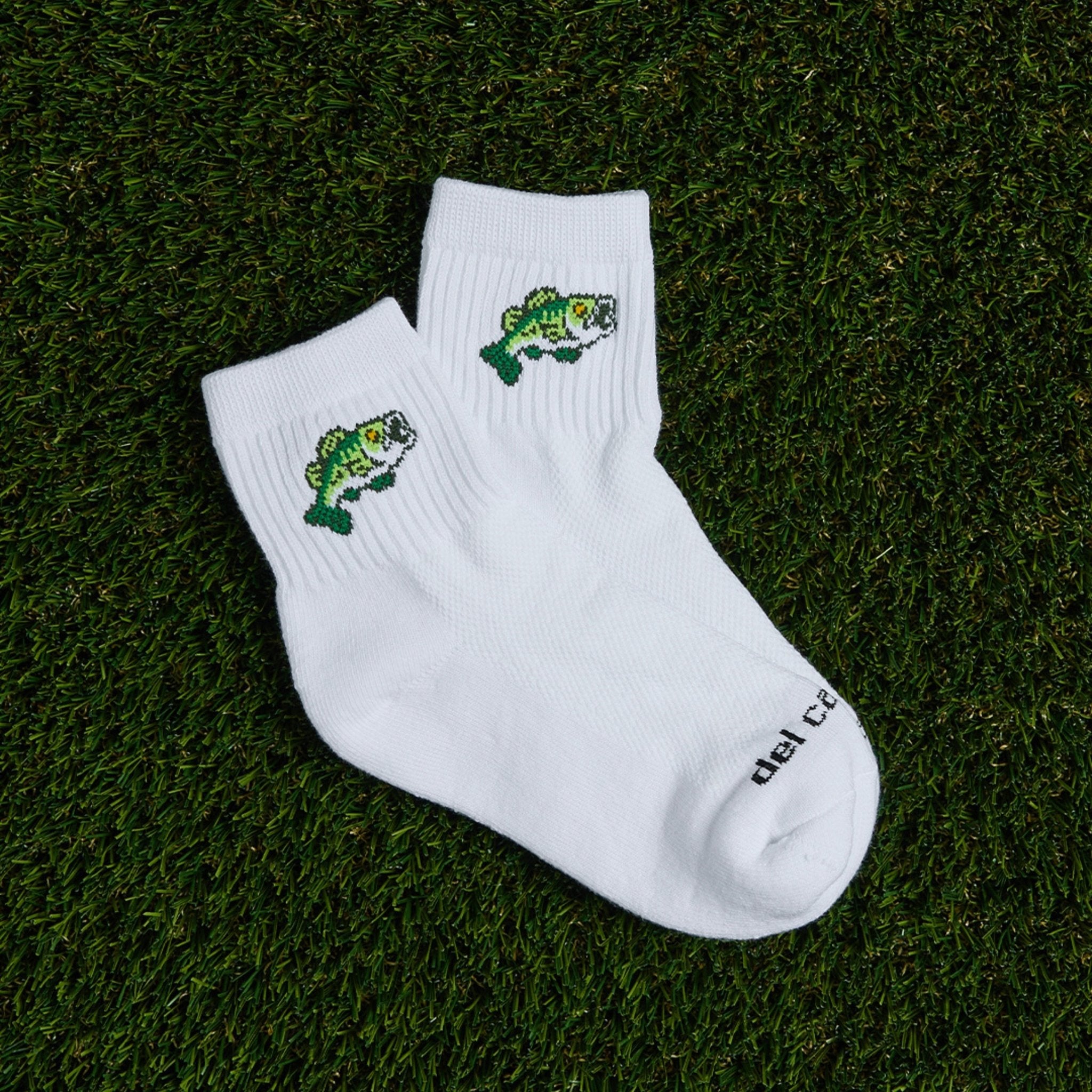 Del Campo Largemouth Bass socks with green embroidered bass, laid on grass