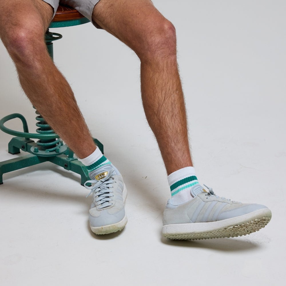 Man wearing white Del Campo Golf Seaside Stripes socks with green and turquoise stripes, posed on exercise equipment. | men, lifestyle, product