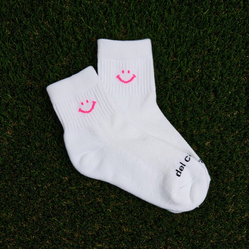 White Del Campo Golf socks with bright pink smiley face design on grass. | product, on-course
