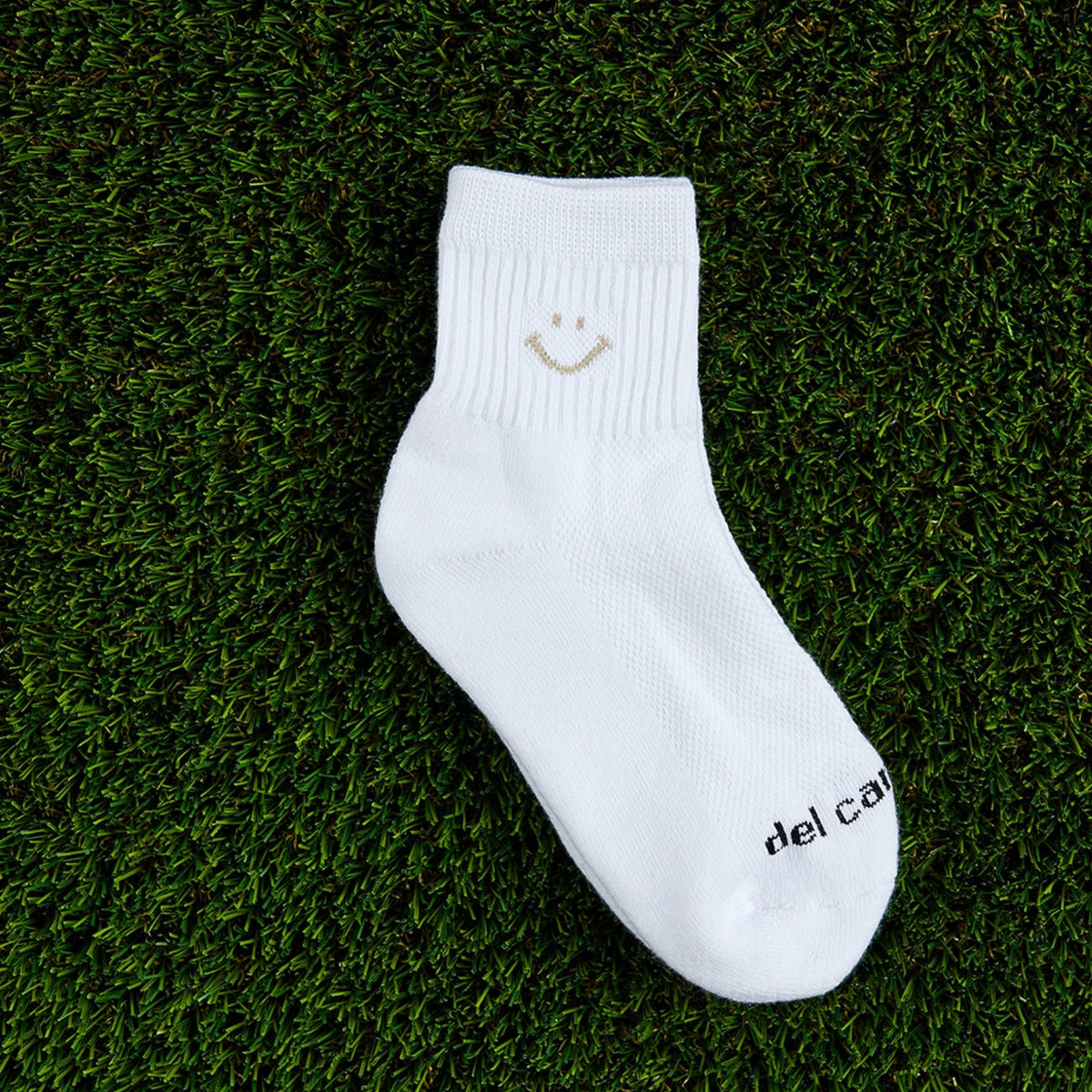 Del Campo Oatmeal Smiley golf socks, flat lay on grass