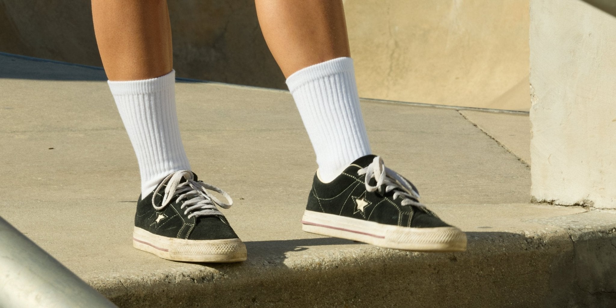 Person wearing white Blank Crew socks with black sneakers on a concrete surface. | lifestyle, men