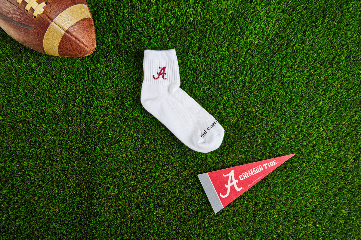 Officially licensed Del Campo Alabama Crimson Tide socks laid out on turf.