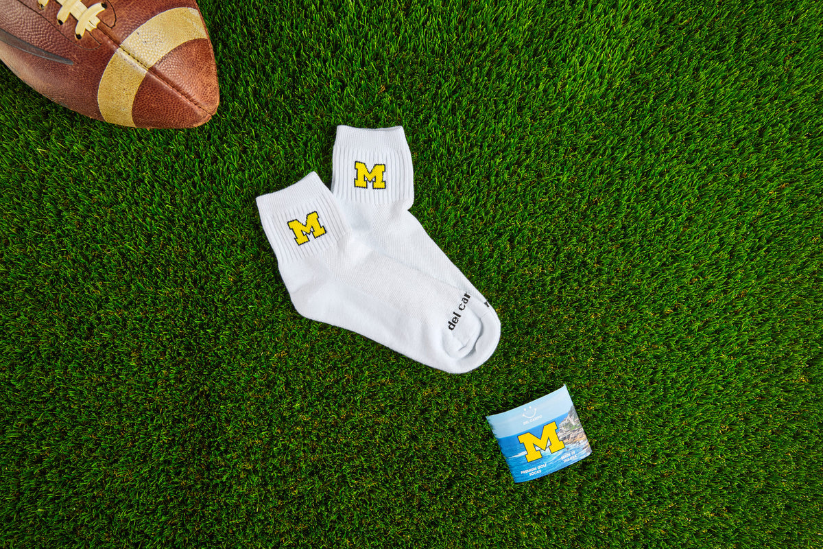 Officially licensed Del Campo Michigan Wolverines socks laid out on turf.