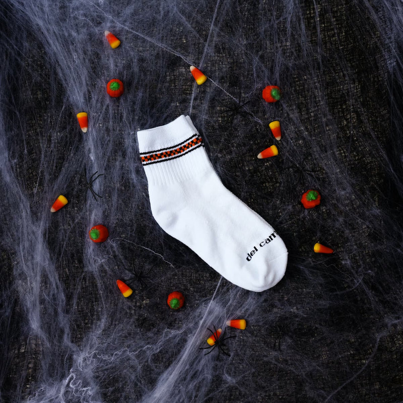 Black and orange checkered stripe sock on a spiderweb with candy corn