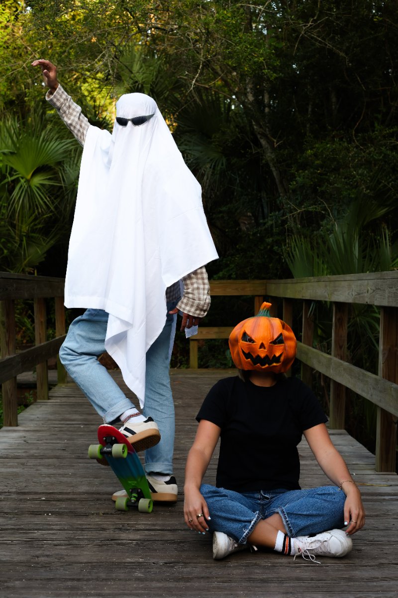 Ghost in sunglasses on a skateboard beside a friend in a jack-o'-lantern mask, both in Halloween stripe socks