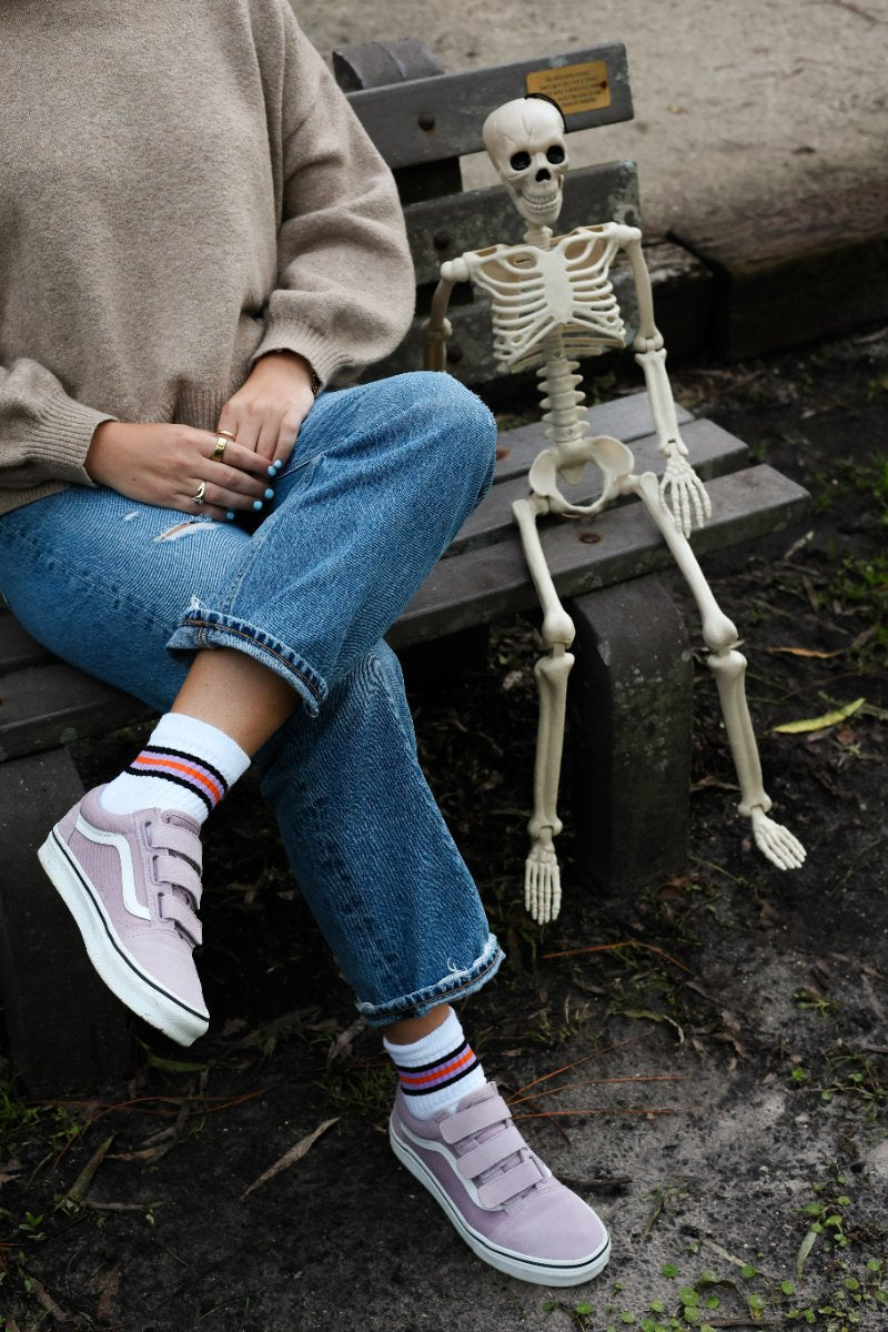 Woman on a bench beside a toy skeleton, wearing Del Campo Halloween stripe socks
