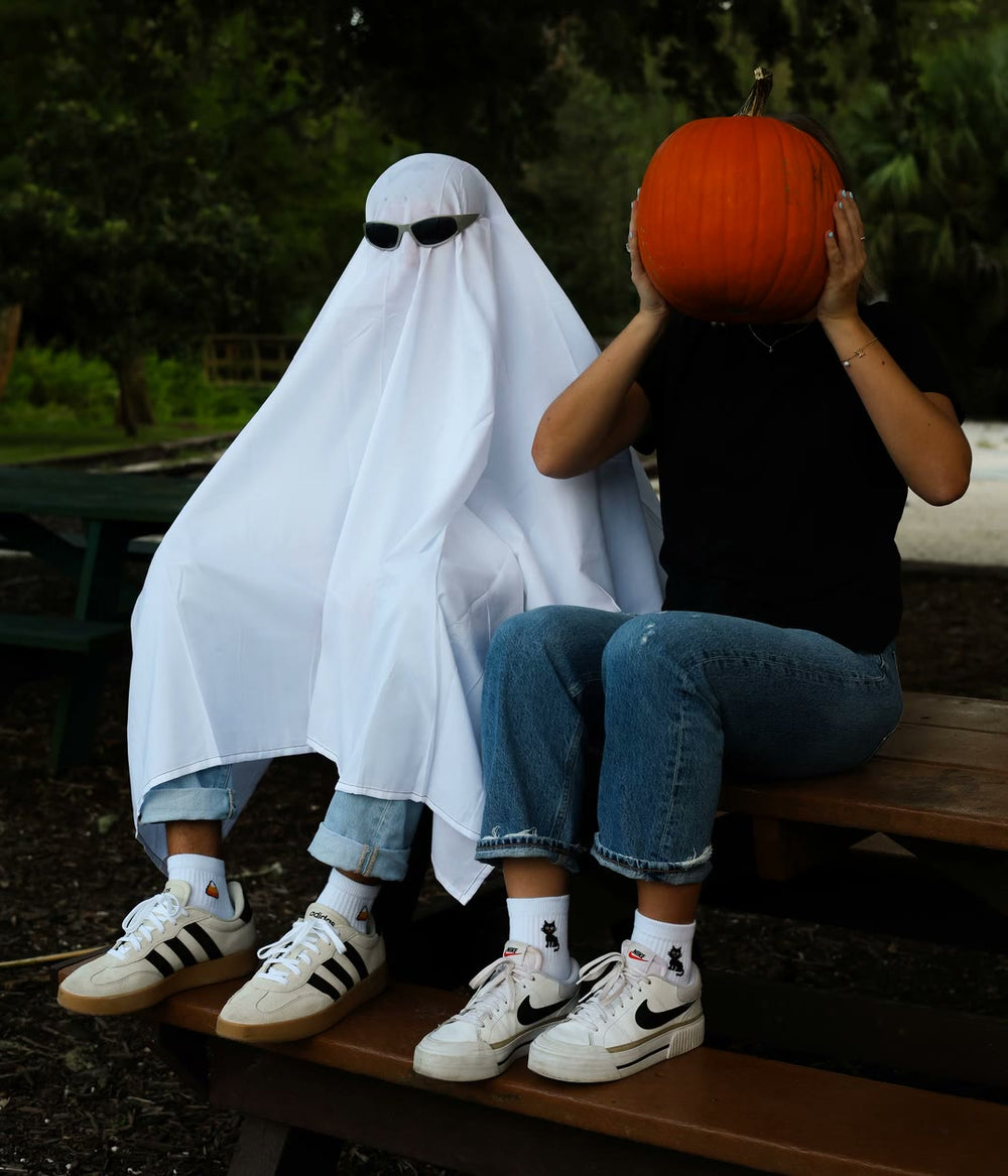 A ghost in sunglasses and a pumpkin head sitting on a bench in Del Campo Halloween socks